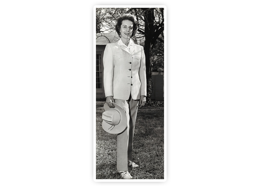 A young Jane Chilton Justin posing in the grass holding a cowboy hat and wearing a business suit.